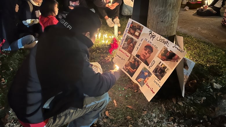 A man kneels down by a vigil sign. 