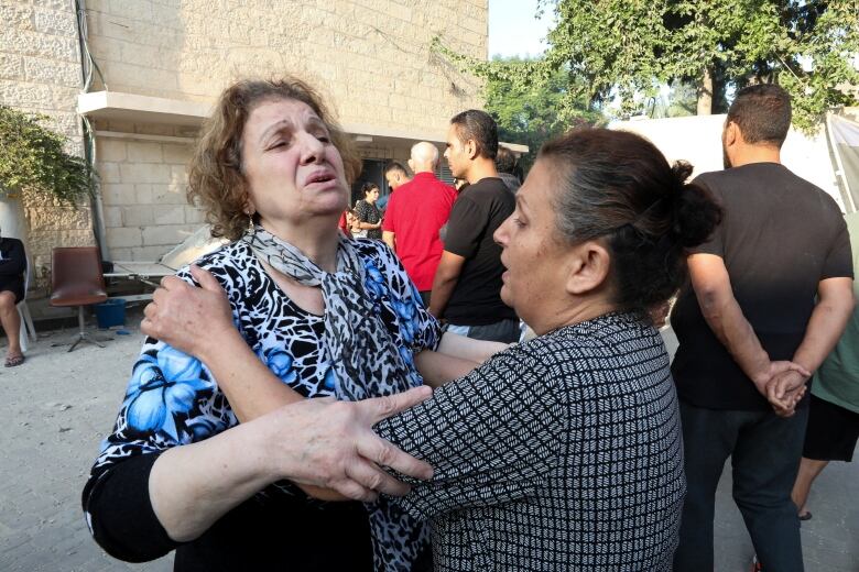 One woman grabs another, who appears distressed, in an outdoor setting.