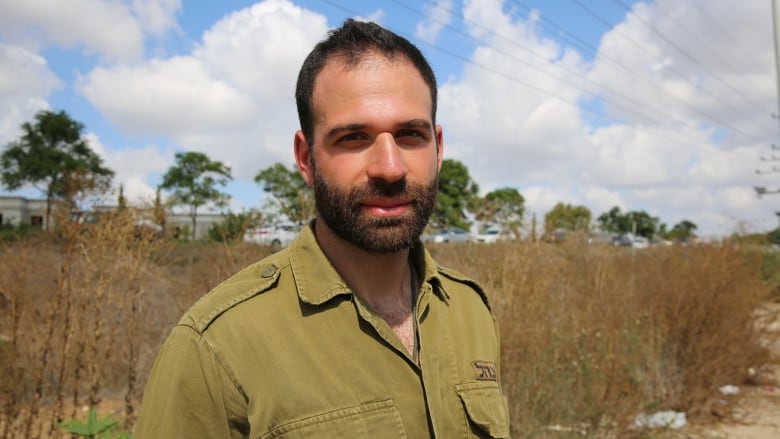 A portrait of a bearded man in an olive-green shirt standing outside.