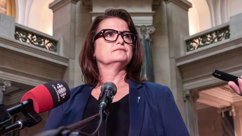 A woman in a black shirt and blue jacket stands in front of a microphone. 