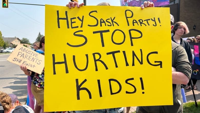 A person in a crowd holds a yellow sign reading 