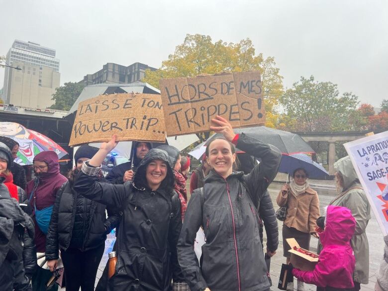 Women stand in the street under the rain. They hold up signs.