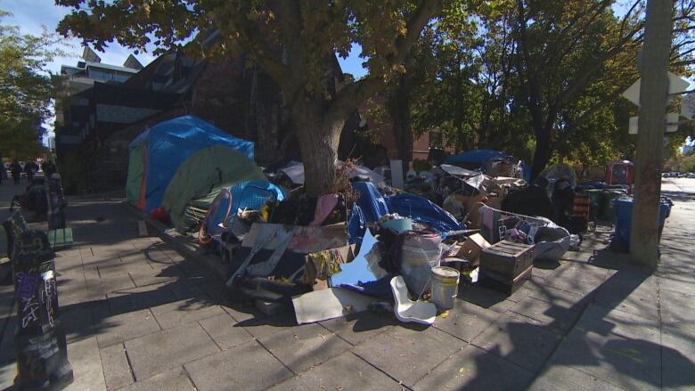 An encampment, featuring items like tents and other belongings, is seen on a sidewalk outside of a church.