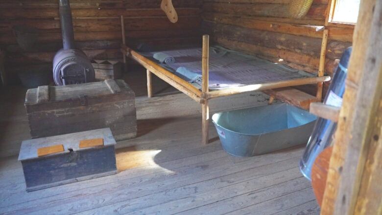 The inside of a wooden cabin with a wooden bed, a fireplace and a metal basin.