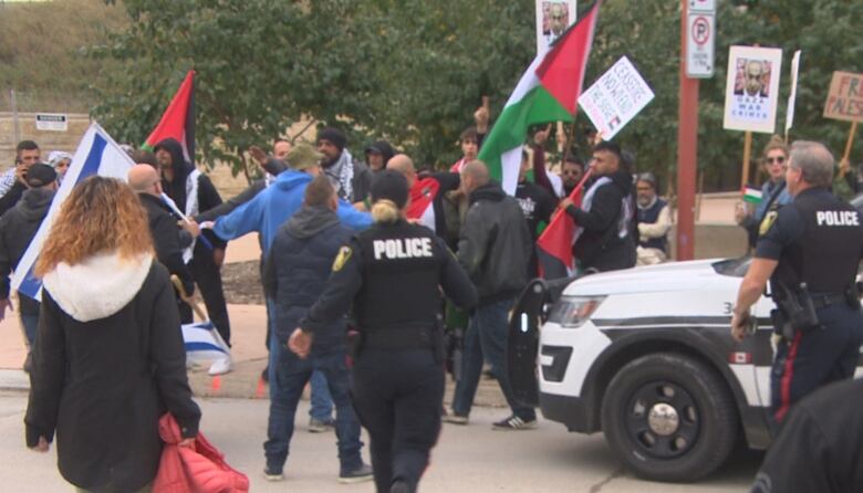 Police rush into a scene where people are yelling at each other and holding flags