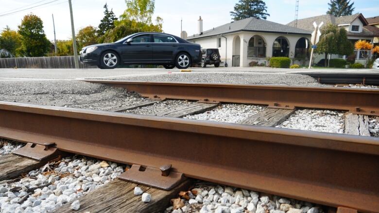 A rail crossing at a street in Windsor with homes in the background and a car passing by. 