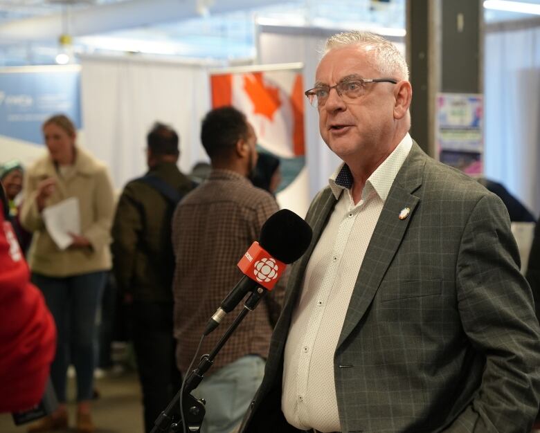 a man wearing a grey jacket and white shirt stand in front of a microphone