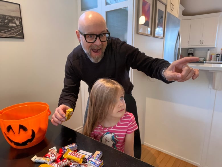 A man with glasses points to distract a child while stealing a piee of Halloween candy with his other hand.