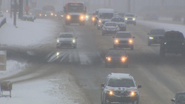 snow covered vehicles are seen travelling on a snowy street