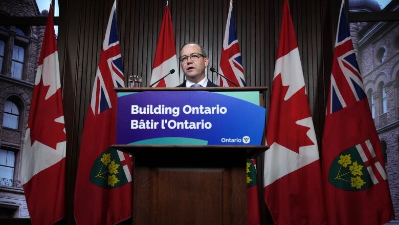 A man speaks at a podium, with the sign 