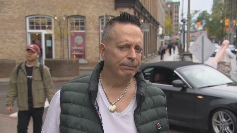 A man looks at a camera during an interview on a city street in autumn.