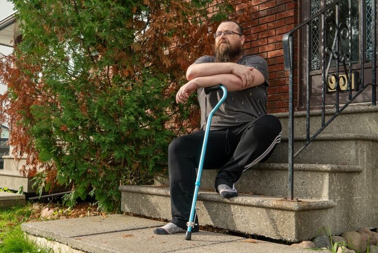 A man with a beard sits on the front steps of a house. 