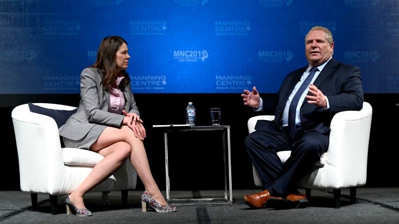 A seated man talks and gestures while a woman leans in, listening.