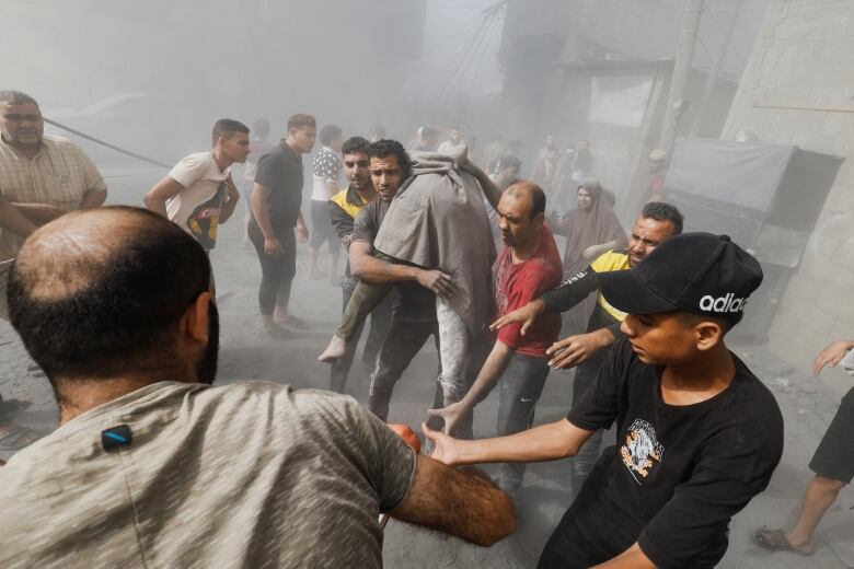 Several people are shown in a hazy scene outside, with one man carrying a person over his shoulder.