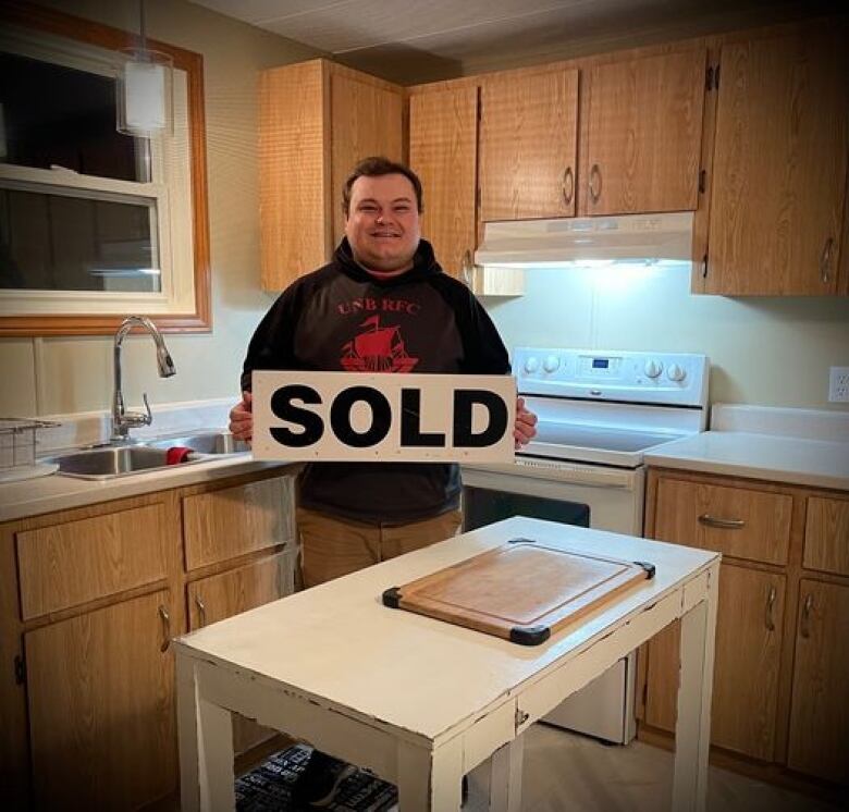 Young man holds a 'for sale' sign in a kitchen