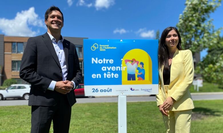 A youg man and women, both in business attire, stand on either side of a colourful sign that refers to the future.