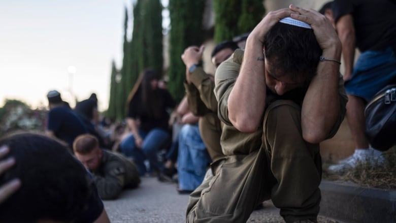 People crouch in the street and cover their heads with their arms.