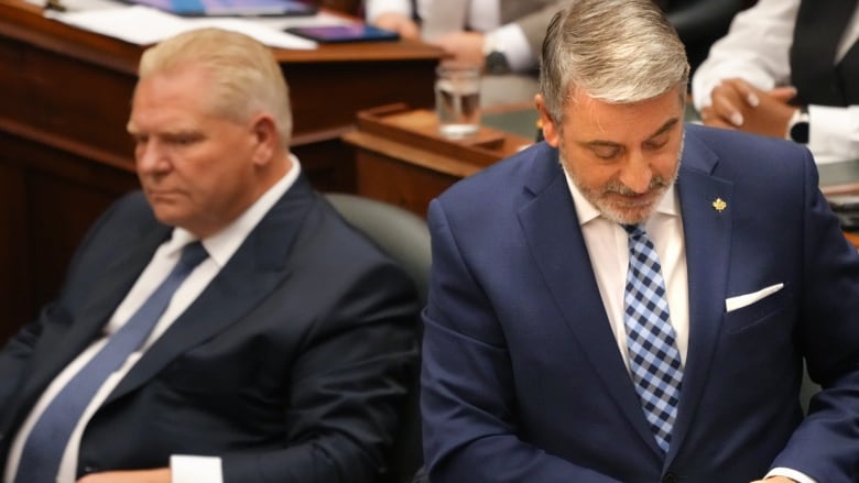 Paul Calandra stands next to a seated Doug Ford in the Legislature. 