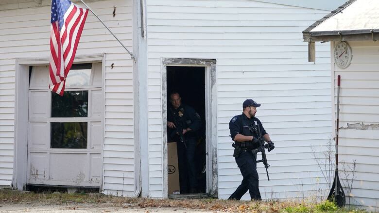 Armed police officers exit a house as a U.S. flag hangs over the doorway.