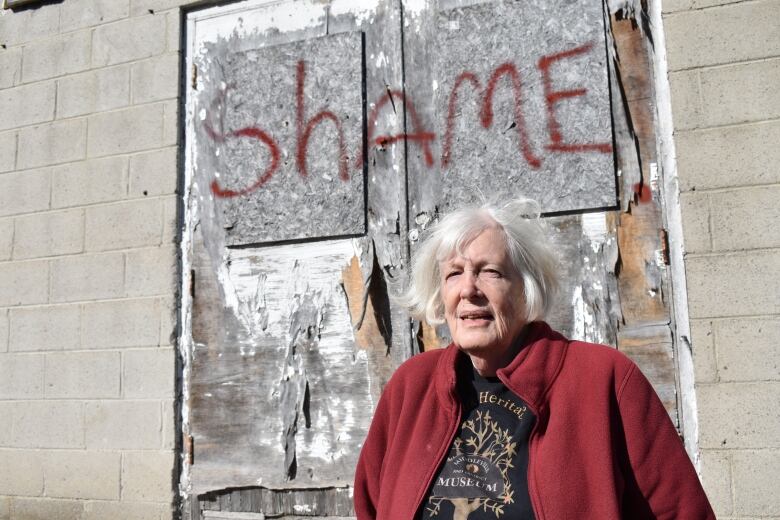 A woman stands in front of a graffitied wall.