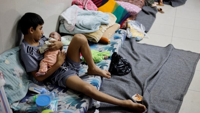 A child holds a baby while sitting on the floor of a hospital.