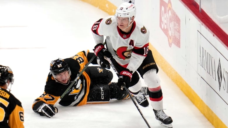 A hockey player skates the puck away from an opponent who has fallen on the ice.