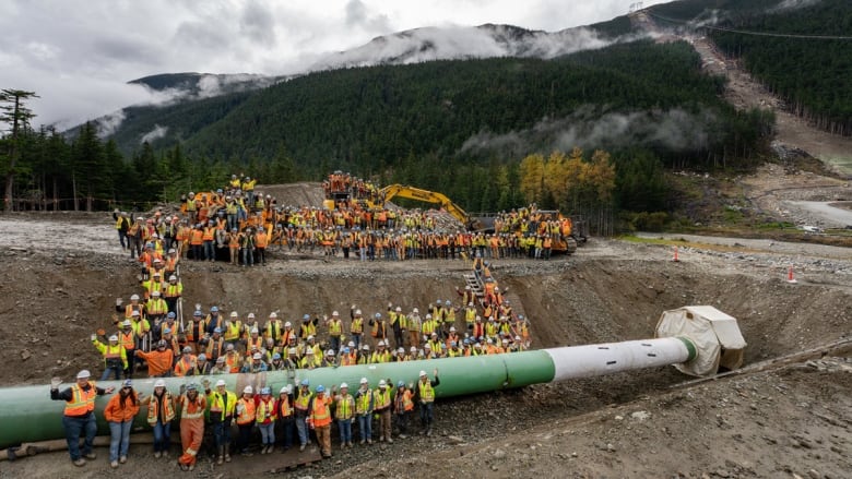 A group of pipeline workers install a pipeline in a massive hole.