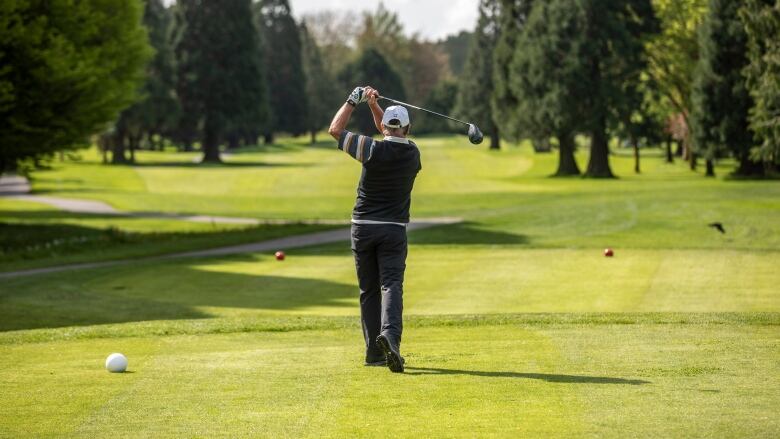 A golfer tees off at a green golf course.