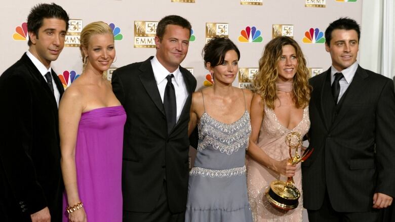 Three men and three women pose with a Emmy award.