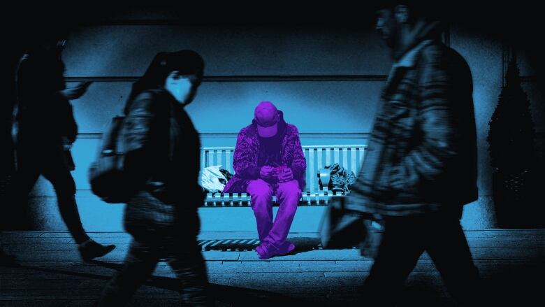 A man sits on a bench as people walk by. 