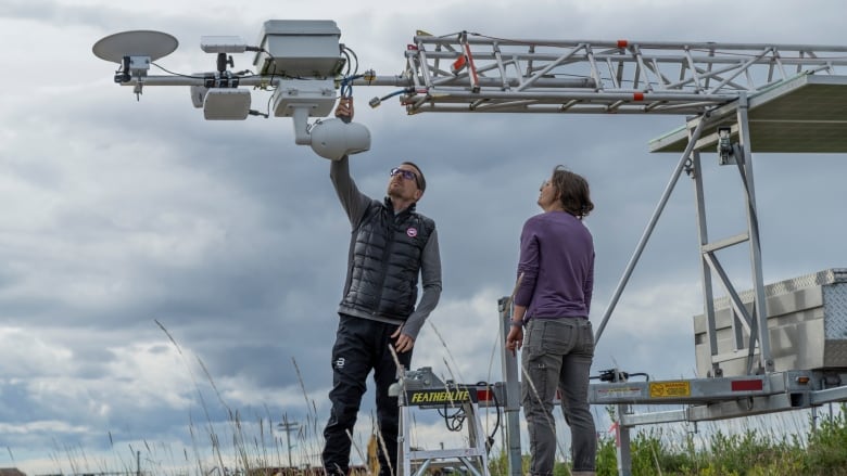 A man and a woman stand underneath a metal contraption in a field. 