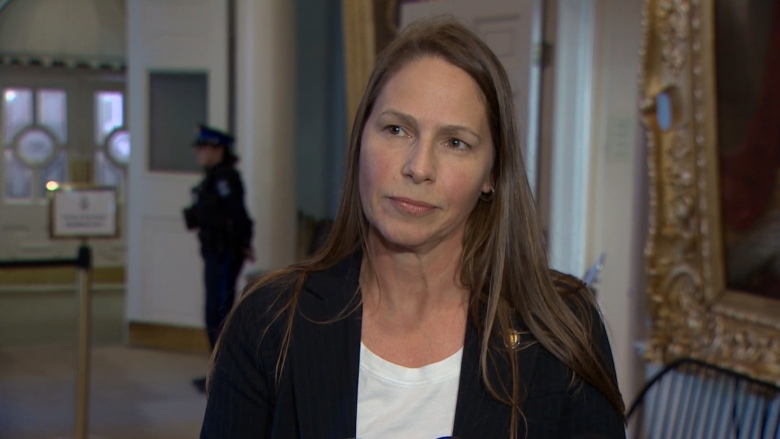 A woman with long, brown hair stands inside Nova Scotia Province House. She wears a white shirt and black blazer