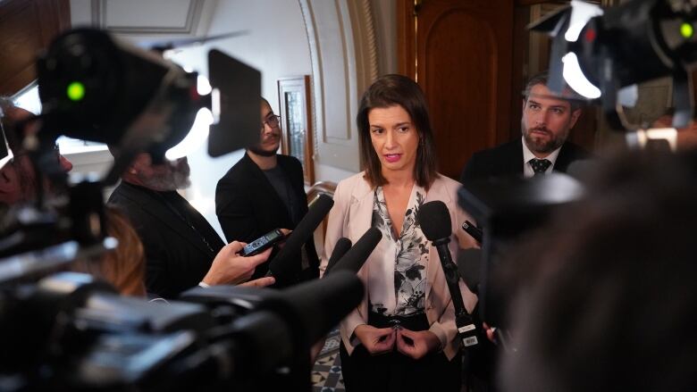 Woman in business attire surrounded by microphones and cameras.