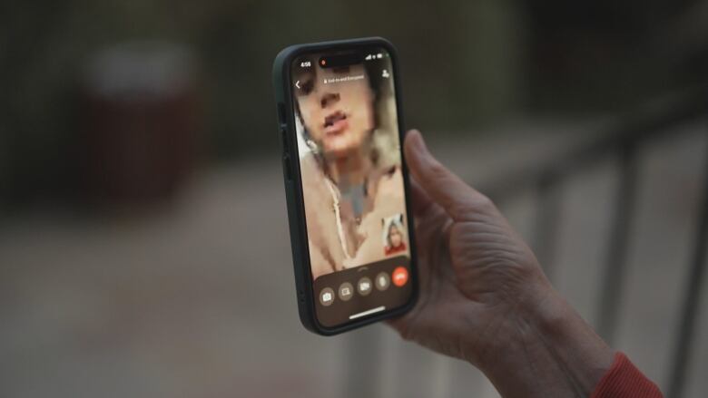 A hand holds a smartphone showing a young woman on a WhatsApp video call