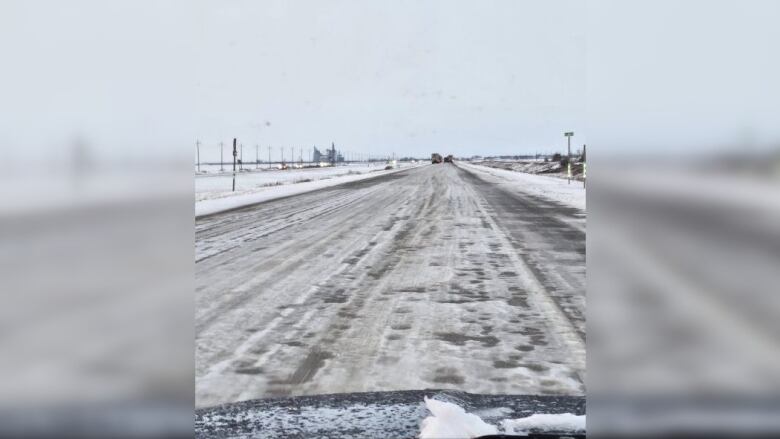 A rutted and icy winter road is seen through the windshield of a vehicle.