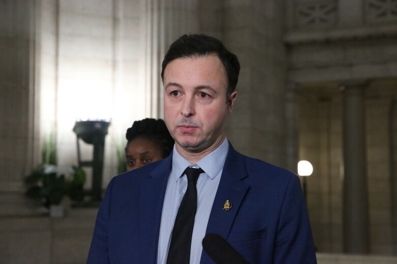 A man in a blue suit stands in a darkened hallway of a legislative building.