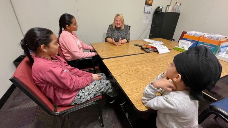 Three children sit around a table with a teacher.