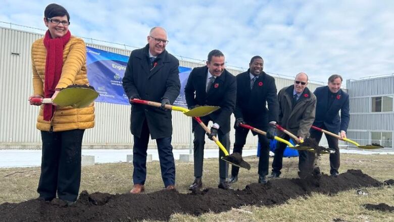 Several people, lined up in a row behind a pile of dirt, carrying shovels with dirt on it.