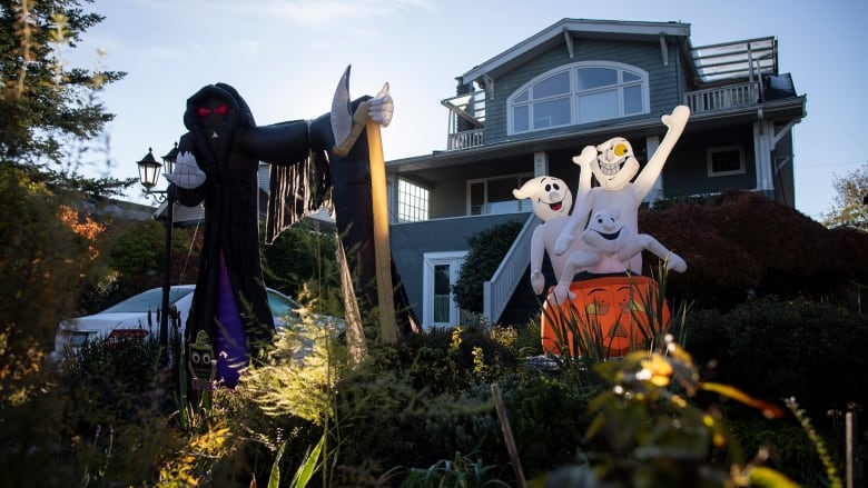 An inflatable grim reaper, and a number of inflatable ghosts arising from a pumpkin, in front of a home.