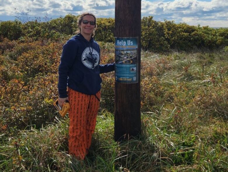 A woman in a hoodie and orange pants standing next to a pole with a poster on it