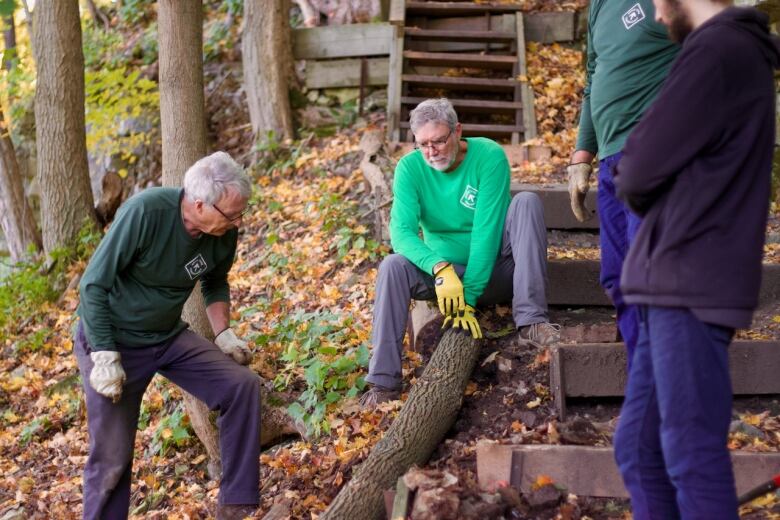 A person sits on a path down a slope holding a log while others look at them. 