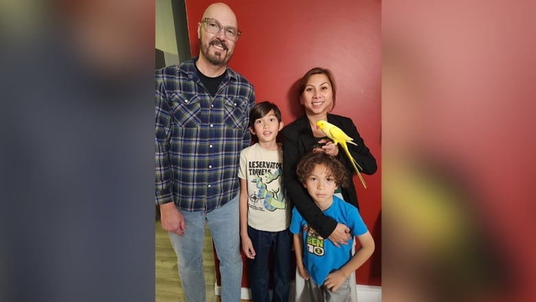 A man, a woman and two children smile. The woman has a yellow bird on her finger.