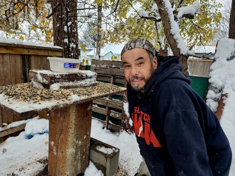 A man stands beside a bird feeder full of birdseed.