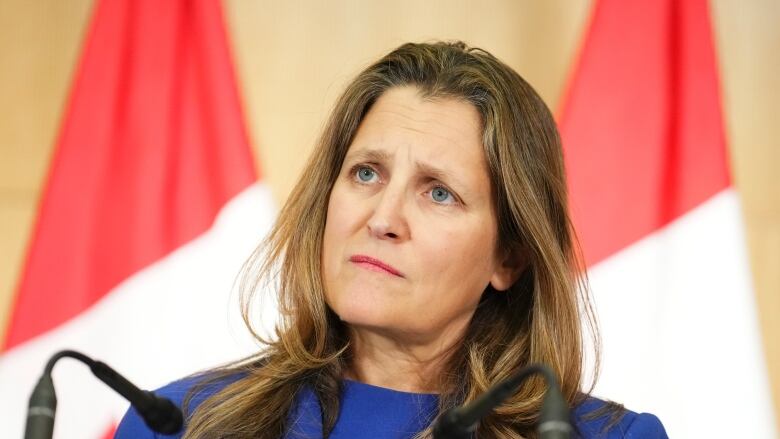 A woman stands at a podium and listens to a question from a reporter, (not shown).