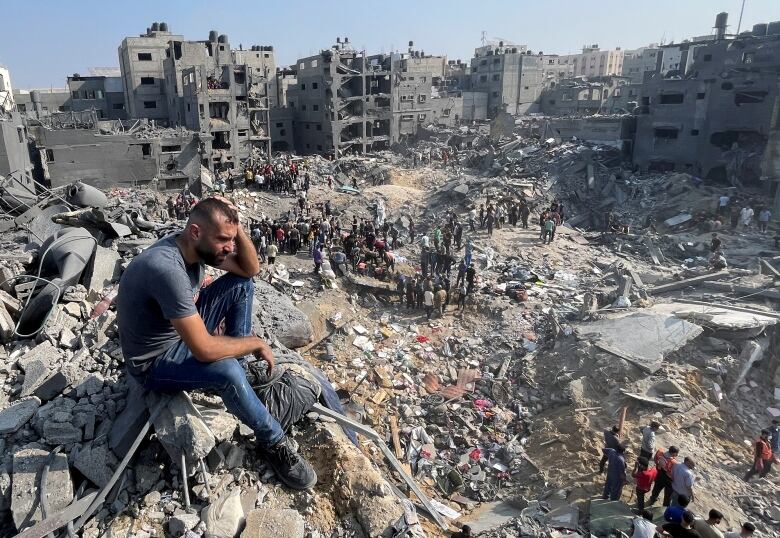 A man sits on top of rubble as people search for survivors after an airstrike.