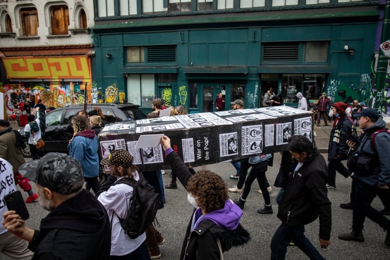 People carry a cardboard coffin in a busy street.