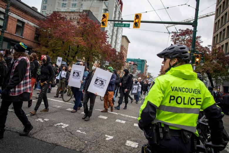 A crowd of people walk on a busy street with a police officer in the foreground.