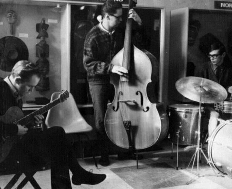 A black-and-white photo of three men playing a guitar, stand-up bass and drums.