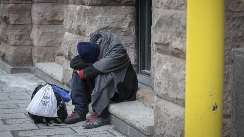 Person covering their face and crouching on the street