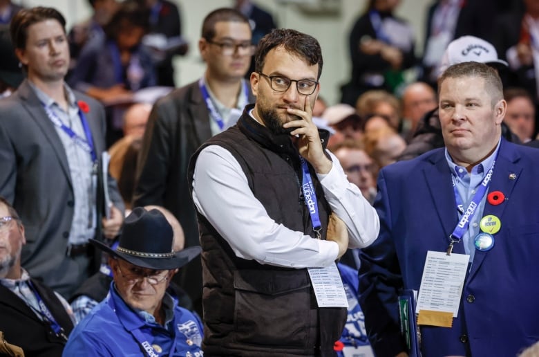 A man wearing a vest overtop a white shirt with a lanyard looks to his right.